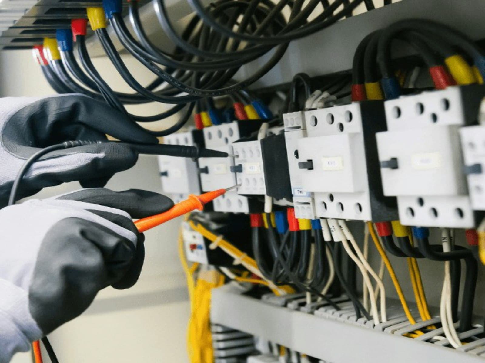 Electrician testing contactors and motor starters in a panel.